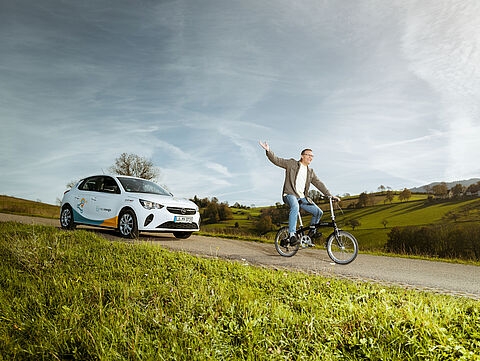 Sharing Auto und Fahrrad Mann auf Fahrrad und dahinter Carsharing Auto von naturenergie