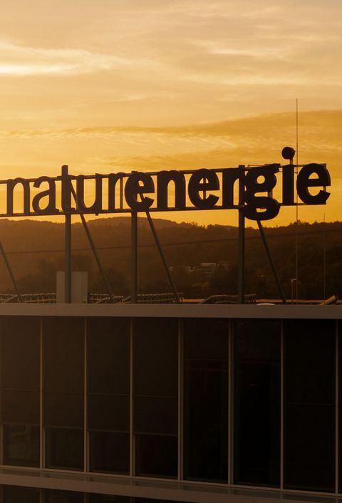 Das Bild zeigt das naturenergie-Logo auf dem Dach des Hauptgebäudes in Rheinfelden bei Sonnenuntergang.