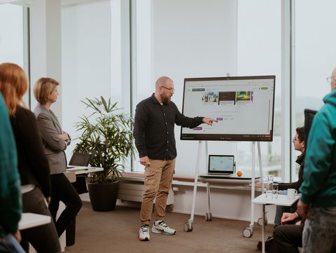Mann hält eine Präsentation vor einer Gruppe von Kollegen in einem modernen Büro.