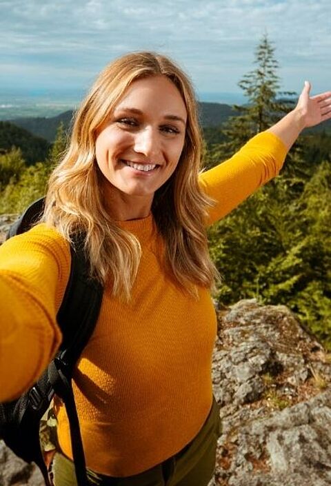 Person mit Rucksack auf Fels in Waldlandschaft Person mit Rucksack macht Selfie auf Felsvorsprung in bewaldeter Landschaft