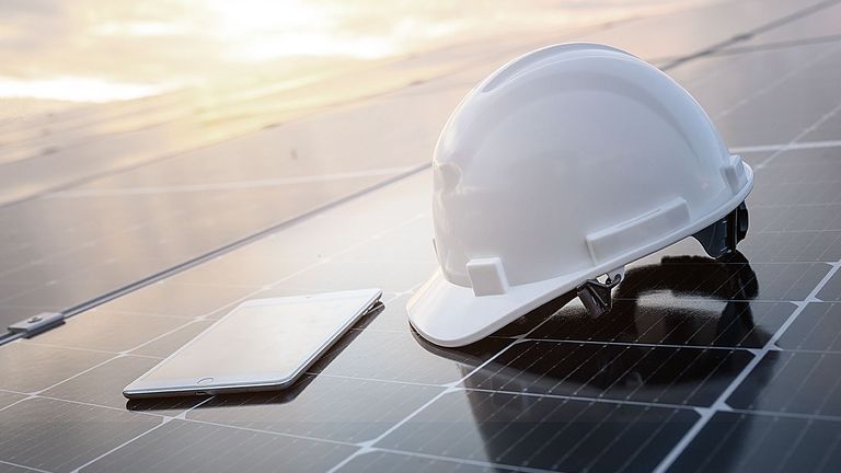 Weißer Bauhelm und ein Tablet auf dem Solarpaneel in einem Photovoltaik-Kraftwerk bei Sonnenaufgang